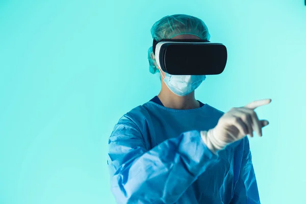 Caucasian surgeon using VR glasses to prepare for the surgery. Monitoring patient simulation. Medium close up studio shot with blue background. — Stock Photo, Image
