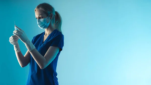Gezondheidszorg concept. Jonge gespecialiseerde arts bereidt anti-coronavirus vaccinatie of antibioticum voor de schoorsteen. Medium studio shot, blauwe achtergrond. — Stockfoto