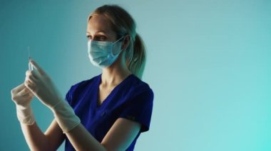 Sağlık sigortası konsepti. Genç doktor, koronavirüs aşısı ya da baca için antibiyotik hazırlıyor. Orta stüdyo çekimi, mavi arkaplan.