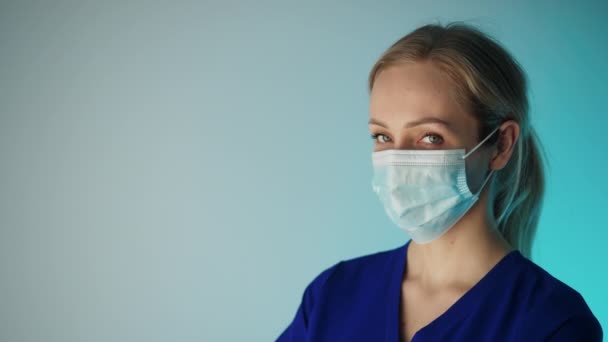 Europeisk kvinnlig sjuksköterska i 30-årsåldern tittar på kameran medan hon bär ansiktsmask som täcker hennes mun och näsa. — Stockvideo
