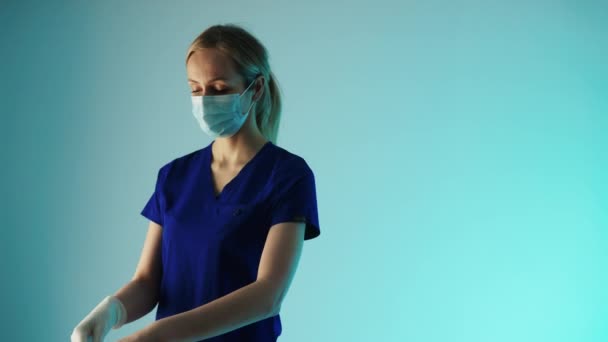 Trabajadora de salud seria poniéndose los guantes, usando máscara quirúrgica para prevenir la propagación de bacterias y virus. — Vídeo de stock