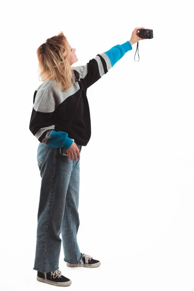 Флюиды 90-х. Девушка делает селфи с винтажной цифровой камерой. Вертикальная студия. Принято. Белый фон. — стоковое фото
