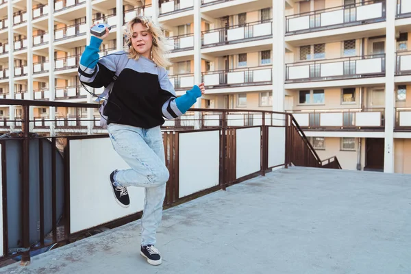 90-talets tonårskoncept. Full utomhus bild av dansande blond-hårig kvinna i 20-årsåldern i säckiga jeans håller sin gammaldags vintage musikspelare. — Stockfoto