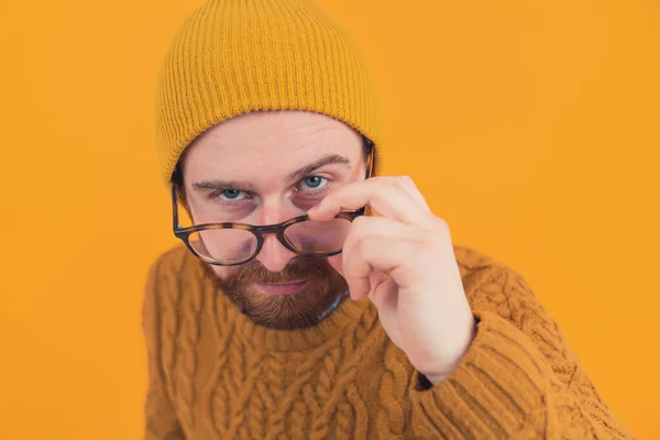 Портрет молодого бородатого кавказца, подозрительно смотрящего, опуская очки, изолированный оранжевый фон — стоковое фото