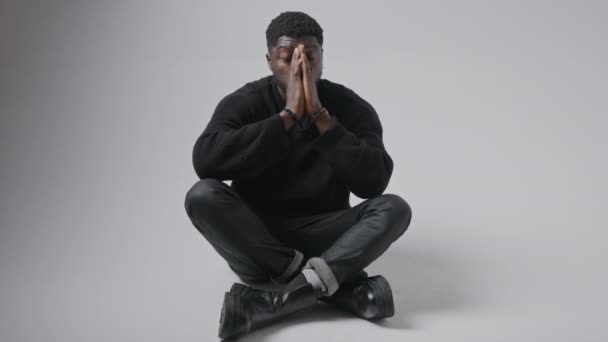 絶望を示す床に座っているハンサムなアフリカ系アメリカ人男性彼の手と頭の灰色の背景コピースペース — ストック動画
