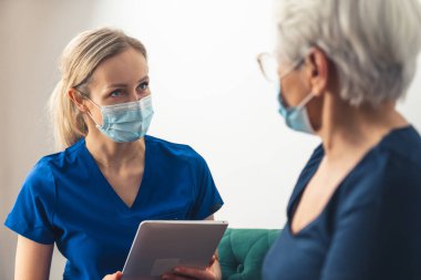 Kafkasyalı kadın doktor, kanepede yaşlı bir kadınla oturuyor. Ev ziyareti kavramı.