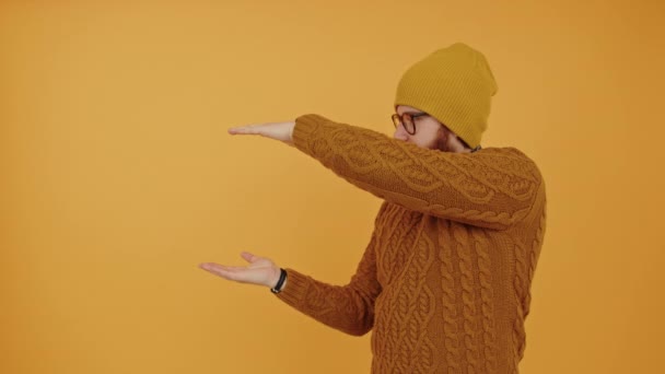 Videoporträt junger bärtiger kaukasischer Mann misst etwas mit seinen Händen und blickt in die Kamera gelber Hintergrund Studio aufgenommen isolierten Kopierraum — Stockvideo