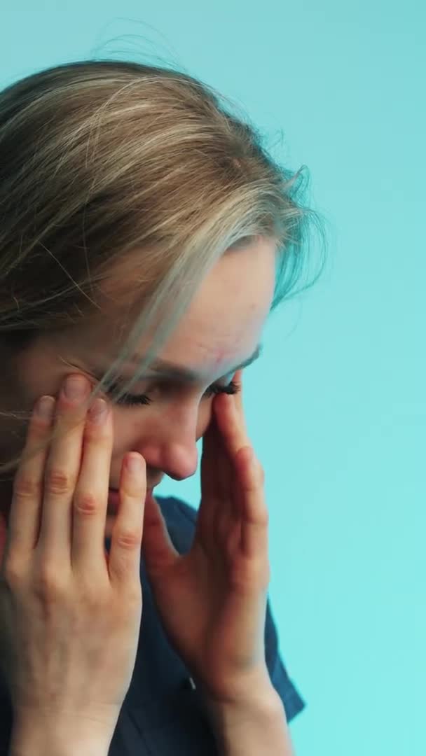 Vertikální video - Smutně vyčerpaná běloška, která se dotýká své tváře na modrém pozadí. Studio shot. — Stock video