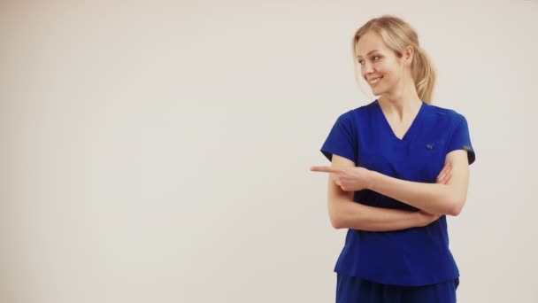 Espaço cópia fundo branco feminino médico cirurgião olhando para o lado e apontando com o dedo e cruzando os braços. — Vídeo de Stock