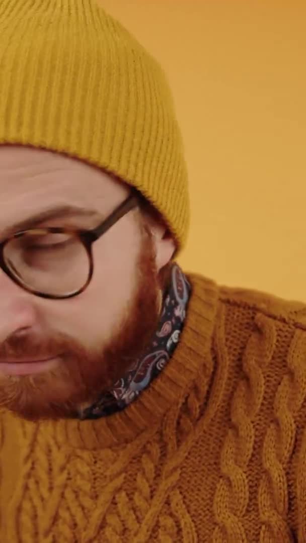 Ung attraktiv europæisk mand ser på kameraet, tager sine briller og blinker gul baggrund studie skudt lodret video – Stock-video
