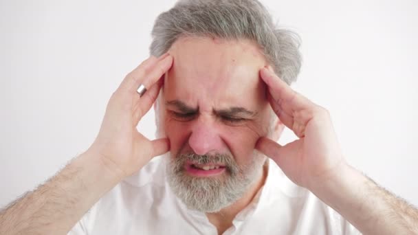 Starší muž je viditelně v bolestech, protože obrovská bolest hlavy má, bílé pozadí, zblízka záběr — Stock video