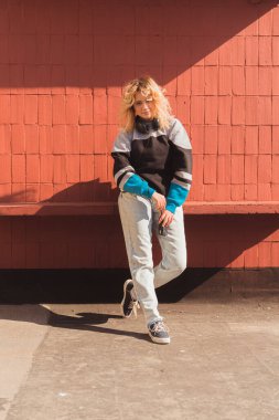 Tuğla duvarın üzerinde poz veren genç sarışın yaratıcı ve eski model analog kamerasını elinde tutuyor. Dikey çekim.