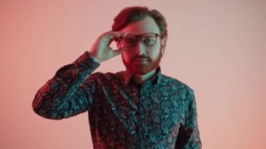 Genç, yakışıklı, sakallı, beyaz adam gözlüklü portresini çıkarıyor. Pembe gradyan arka plan stüdyosu. 