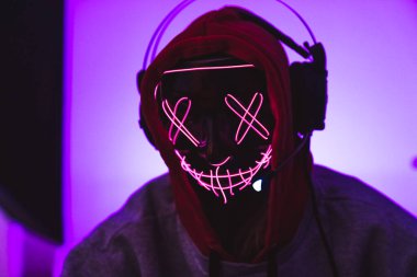 Maskeli, kulaklık takan ve kapüşonlu bir programcı. Pembe arkaplan.