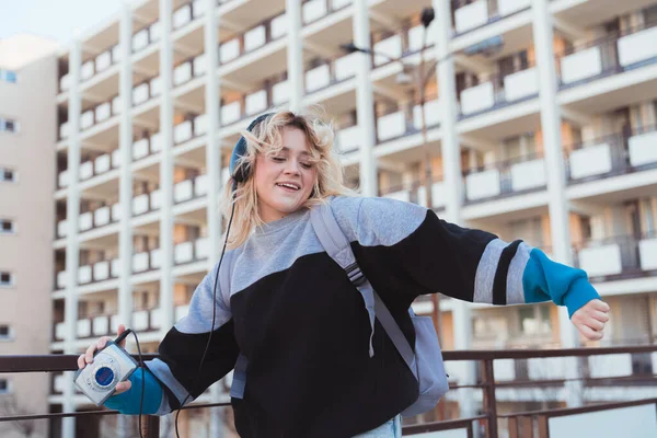 Ung europeisk blond-hårig hipster flicka lyssnar på musik på hörlurar och dans. Gammaldags teknikkoncept. — Stockfoto