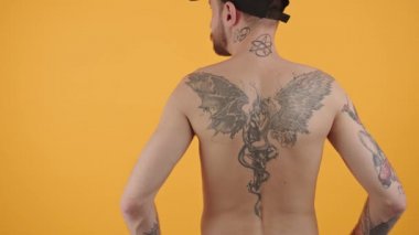 Orta yaşlı beyaz bir adam sarı arka planda dövmesini kameraya gösteriyor. Modern dövme kavramı.