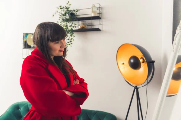 Femme client européenne confiante se regardant dans le miroir tout en essayant manteau d'hiver rouge. — Photo