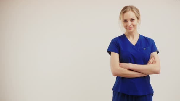 Agente de santé blonde positive en uniforme bleu foncé regardant la caméra et croisant les bras. Isolé moyen studio tourné. — Video