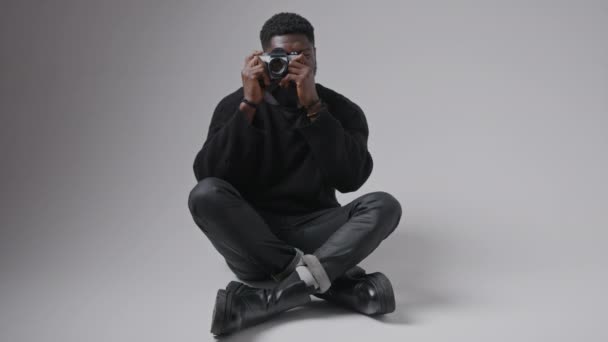 African American man sitter benen korsade på golvet och ta ett foto med kameran full bild studio sköt grå bakgrund kopiera utrymme — Stockvideo
