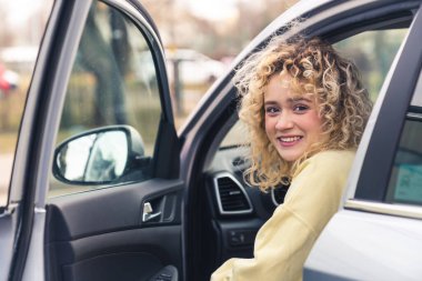 Çekici sarı kıvırcık saçlı kadın yeni araba portresinin sürücü koltuğunda oturuyor. 