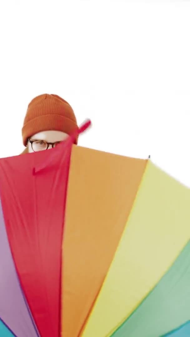 European hipster spins colourful umbrella in his hands and hides behind it white background isolated vertical video copy space studio shot — Stock Video