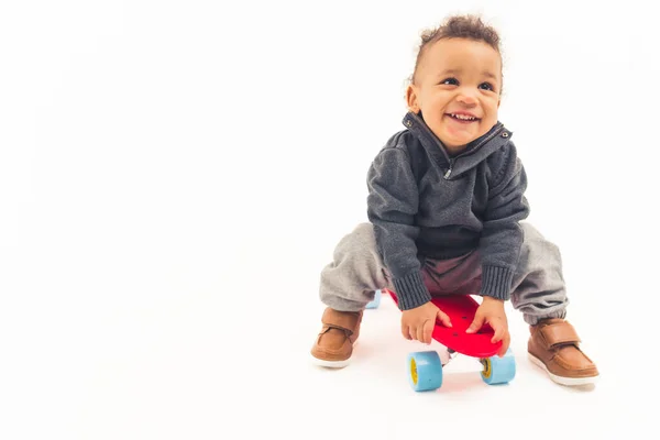 Joyeux bambin interracial mignon en studio jouant avec mini skateboard rouge et riant sur fond blanc. — Photo