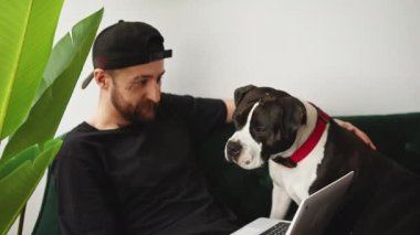 Kafkasyalı, sakallı, orta yaşlı bir adam evden çalışıyor. Kanepesinde oturuyor, büyük, neşeli bir köpekle..