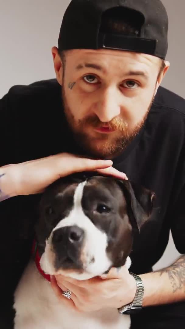 Portrait vertical en studio d'un propriétaire de chien tatoué caucasien caressant son chien et regardant la caméra. — Video