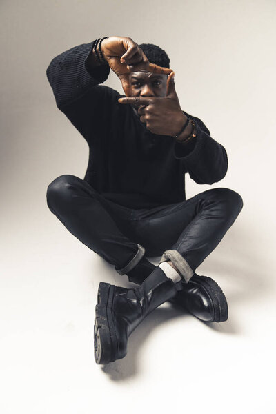 Black man using finger frames sitting - full shot. High-quality photo
