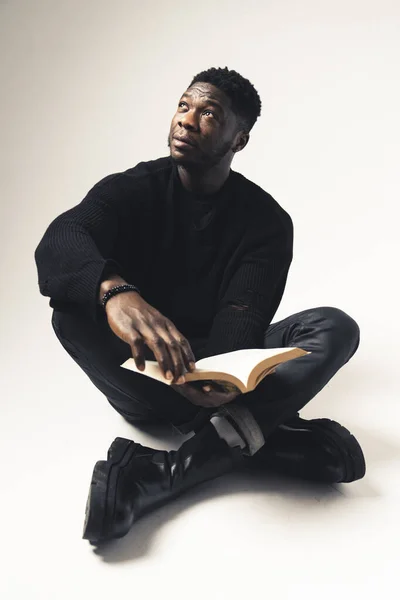 Black men contemplating away with a book seated white background - full shot —  Fotos de Stock