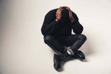 Sıkıntılı bir Afroamerikalı. Elleri başının arkasında. Beyaz arka planda.