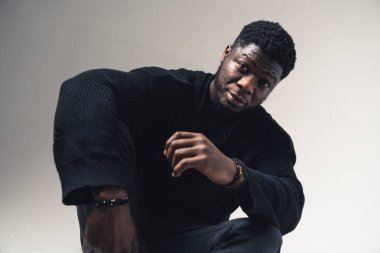 Beyaz arka planda oturan ciddi ifadeli Amerikalı siyahi adamlar.