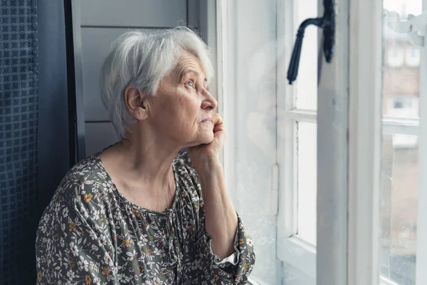 Sad European grandma looking out of the window — Stockfoto