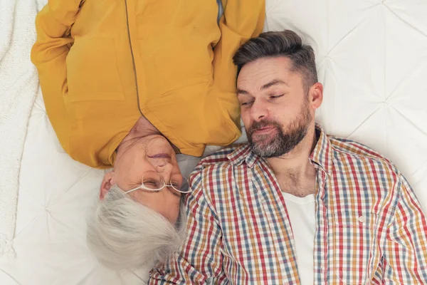 Happy grandson laying down with his retired grandmother and looking at her in a funny way — Foto de Stock
