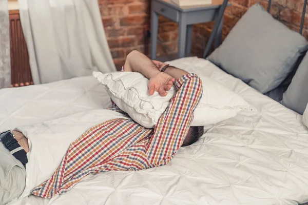 Kafkasyalı yorgun bir adam yatağına uzanmış ve yüzünü beyaz yastıkla örtmüş.