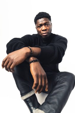 Siyah, göz korkutucu, elleri önde beyaz arka planda oturan adam.