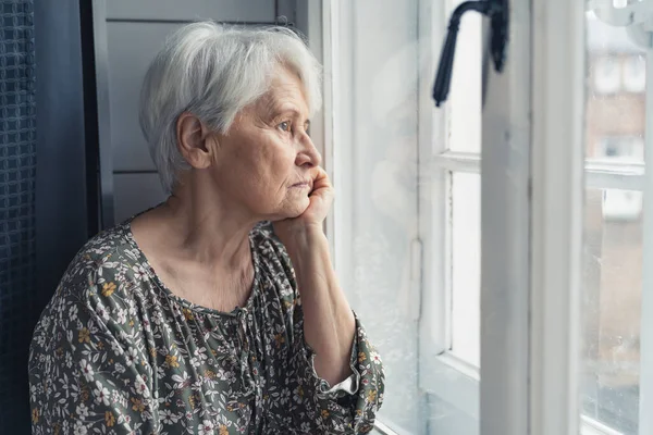Ensam pensionär sitter i köket och tyvärr tittar ut genom fönstret — Stockfoto
