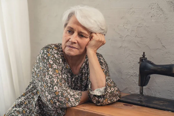 Одинокая европейская пожилая леди думает о грустных вещах и трогает свои седые волосы — стоковое фото