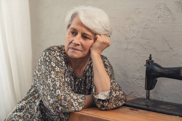 lonely European elderly lady thinking about sad things and touching her grey hair 