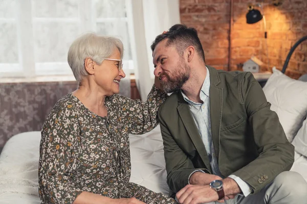 Medelålders kaukasiska affärsman gör dumma ansikten och få sin äldre gråhåriga mor att skratta — Stockfoto
