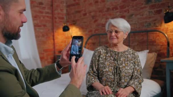 Középkorú kaukázusi vállalkozó fényképez idős ősz hajú anyjáról okostelefonjával — Stock videók