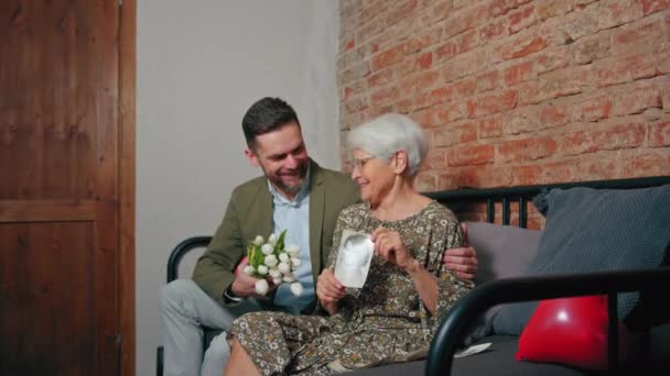 Memories about youth presented by elderly content retired grandmother holding a photo of her in her 20s and sitting next to her adult son — Stock Video