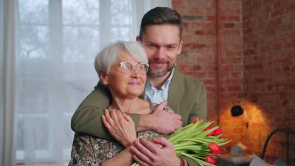 Medio colpo di anziana nonna felice con il suo nipote di mezza età che tiene fiori e celebra la giornata dei nonni — Video Stock