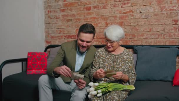 Madre jubilada anciana caucásica y su hijo de mediana edad celebrando el día de las madres sentado en un sofá y mirando viejas fotografías y recuerdos — Vídeos de Stock