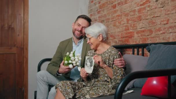 Kaukasische familieleden vieren grootouders dag kijken naar camera grootmoeder met een fotografie van haar jongere zelf — Stockvideo