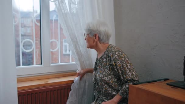Кавказская грустная одинокая задумчивая пожилая женщина с короткими седыми волосами и морщинистым лицом, смотрящая в окно — стоковое видео