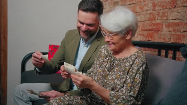 Mãe aposentada europeia ri alto enquanto olha para fotografias antigas e comemora o Dia das Mães com seu filho de meia-idade — Vídeo de Stock