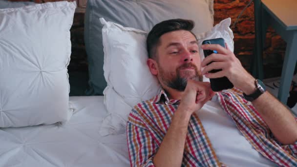 Sorrindo bonito homem europeu usando seu telefone e conversando com seus amigos através de mídias sociais — Vídeo de Stock