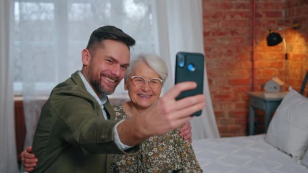 Gelukkig grijnzend oudere moeder en haar middelbare leeftijd duizendjarige zoon het nemen van een domme foto van de twee van hen — Stockvideo