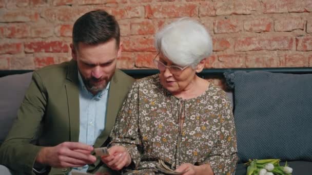 Energiczna stara siwowłosy kobieta chętnie myśli o przeszłości i pokazuje jej dorosły wnuk stare zdjęcia w Dniu Dziadków — Wideo stockowe